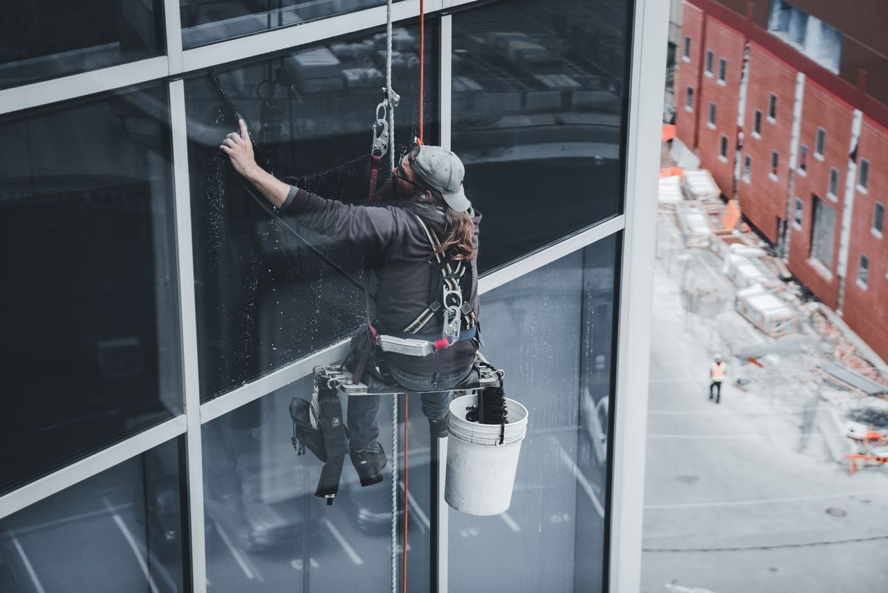 hero-img A worker cleaning skyscraper windows with a harness in an urban setting.